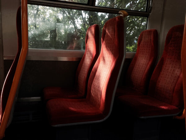 Train interior with two red rows of empty seats and sunlight