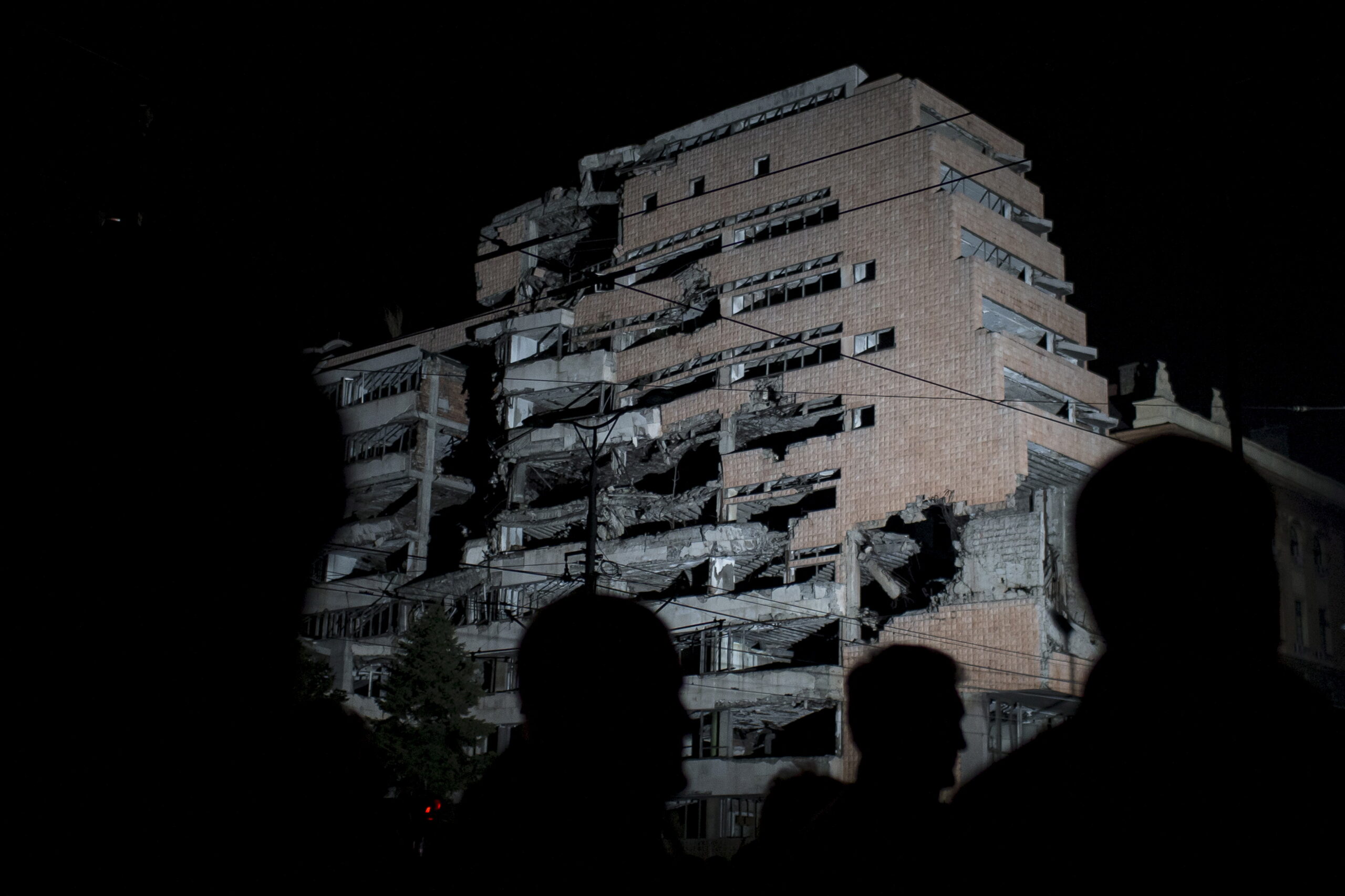 People stand in front of a destroyed military headquaters as Serbia marks the 16th anniversary of the NATO bombing campaign in Belgrade