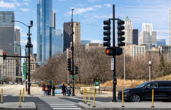 Blick auf eine belebte Straßenkreuzung in Chicago, Illinois, USA, mit fahrenden Autos im Vordergrund und moderner Hochha