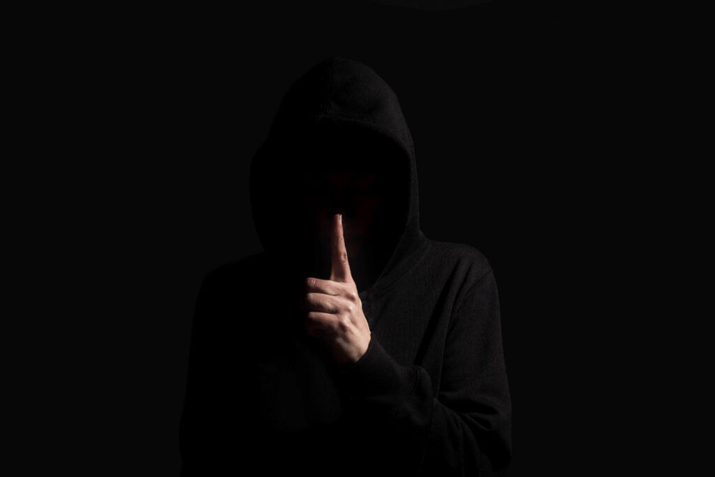 Hacker making silence gesture on dark background wearing hoodie