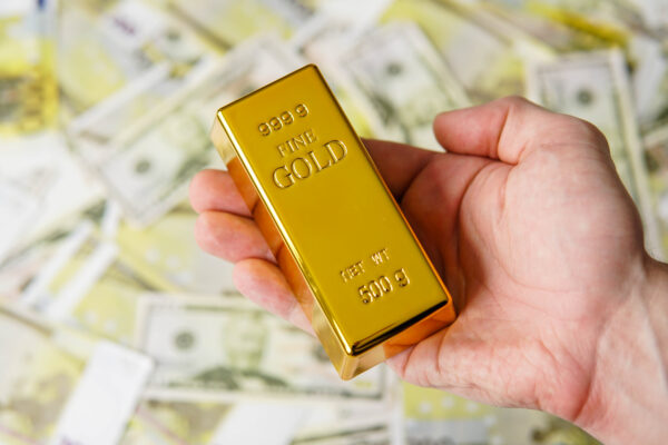 Man holds gold bar on a money banknotes background.