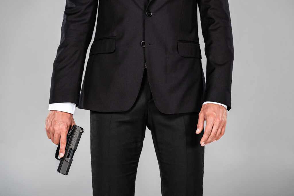 partial view of agent in black suit with gun isolated on grey