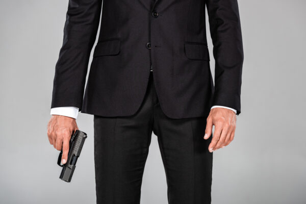 partial view of agent in black suit with gun isolated on grey