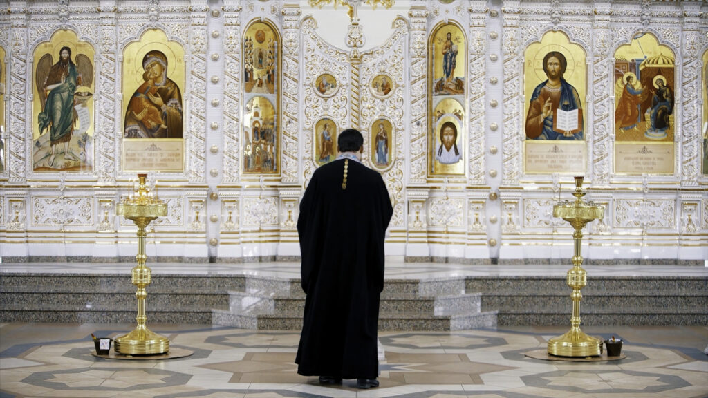 The Iconostasis inside an orthodox church. Video. Rear view of a priest standing in front of the icons with the faces of the saints, concept of religion, interior details inside a church.