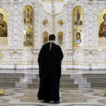 The Iconostasis inside an orthodox church. Video. Rear view of a priest standing in front of the icons with the faces of the saints, concept of religion, interior details inside a church.