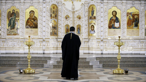 The Iconostasis inside an orthodox church. Video. Rear view of a priest standing in front of the icons with the faces of the saints, concept of religion, interior details inside a church.