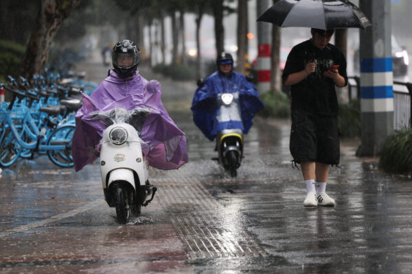 People ride electric scooters in the rain as Typhoon Bavi approaches Wenzhou