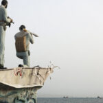 FILE PHOTO: A statue of Iranian military members stands as vessels in the Strait of Hormuz are visible near the beach of Bandar Abbas