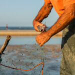 Unrecognizable man tying strings of fishing net