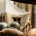 Metal Helmets Of United States Army Infantry Soldier At World War II. Helmets Near Camping Tent In Forest Camp