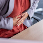 Stomach ache, sick business woman holding hands on stomach close up, female worker at workplace working at table with laptop inside office