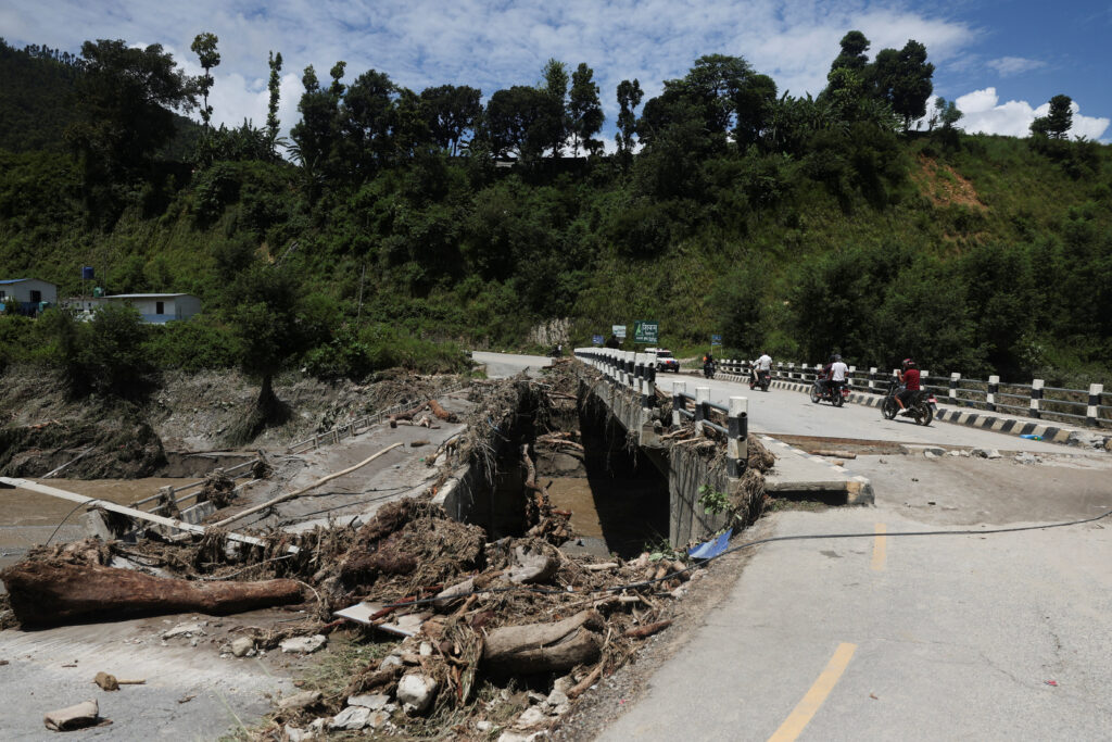 An auto rickshaw drives past a broken bridge following a flash flood in Galchhi