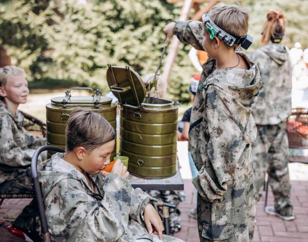 Boy in camouflage relax and drinks tea while playing in laser tag shooting game with a weapon outdoor