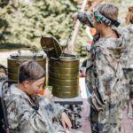 Boy in camouflage relax and drinks tea while playing in laser tag shooting game with a weapon outdoor