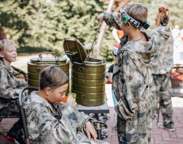 Boy in camouflage relax and drinks tea while playing in laser tag shooting game with a weapon outdoor