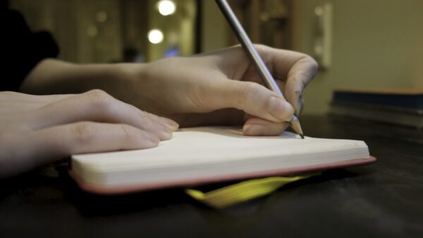 Close-up of woman writing something in notebook in cafe. Concept. Woman writes down something personal or plans day in cozy cafe