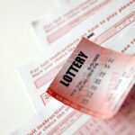 Red lottery ticket lies on pink gambling sheets with numbers for marking to play lottery. Lottery playing concept or gambling addiction. Close up
