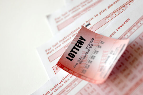 Red lottery ticket lies on pink gambling sheets with numbers for marking to play lottery. Lottery playing concept or gambling addiction. Close up