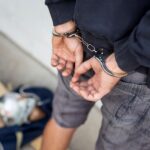 handcuffed-man-standing-by-bag-on-sidewalk-2026-03-24-04-02-49-utc