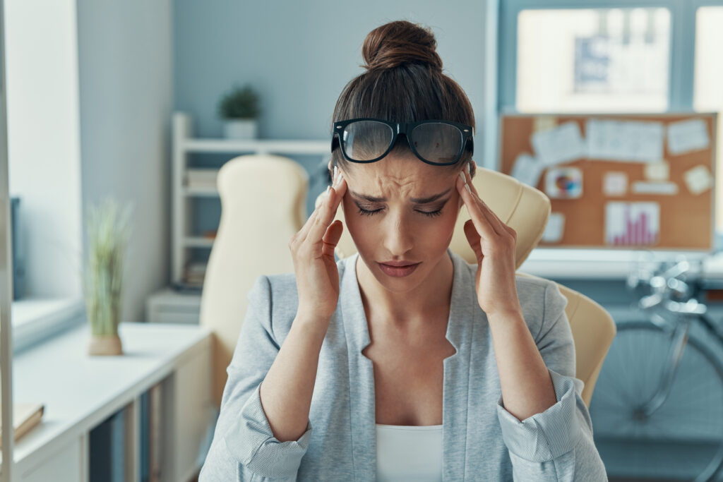 Stressed young woman in smart casual wear keeping head in hands while sitting in the office