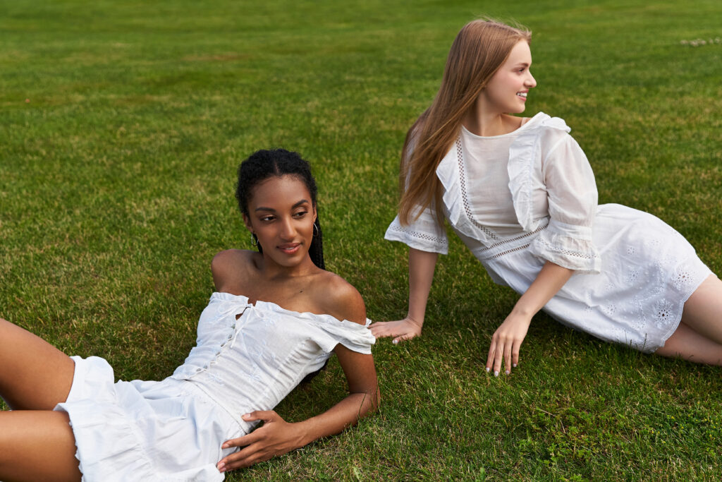 Two young women enjoy each others company while lounging on lush green grass, radiating happiness.