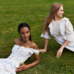 Two young women enjoy each others company while lounging on lush green grass, radiating happiness.